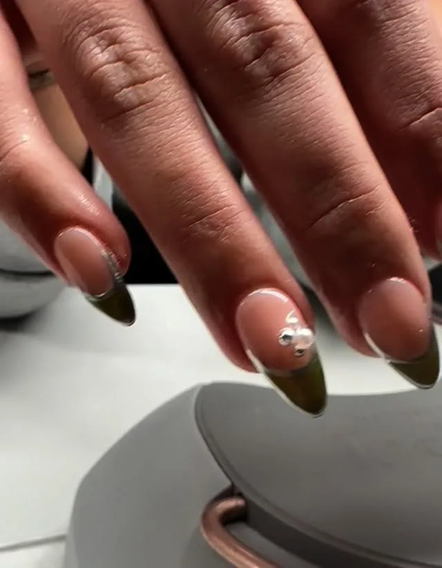 Olive-green French-tip almond nails with a silver charm accent