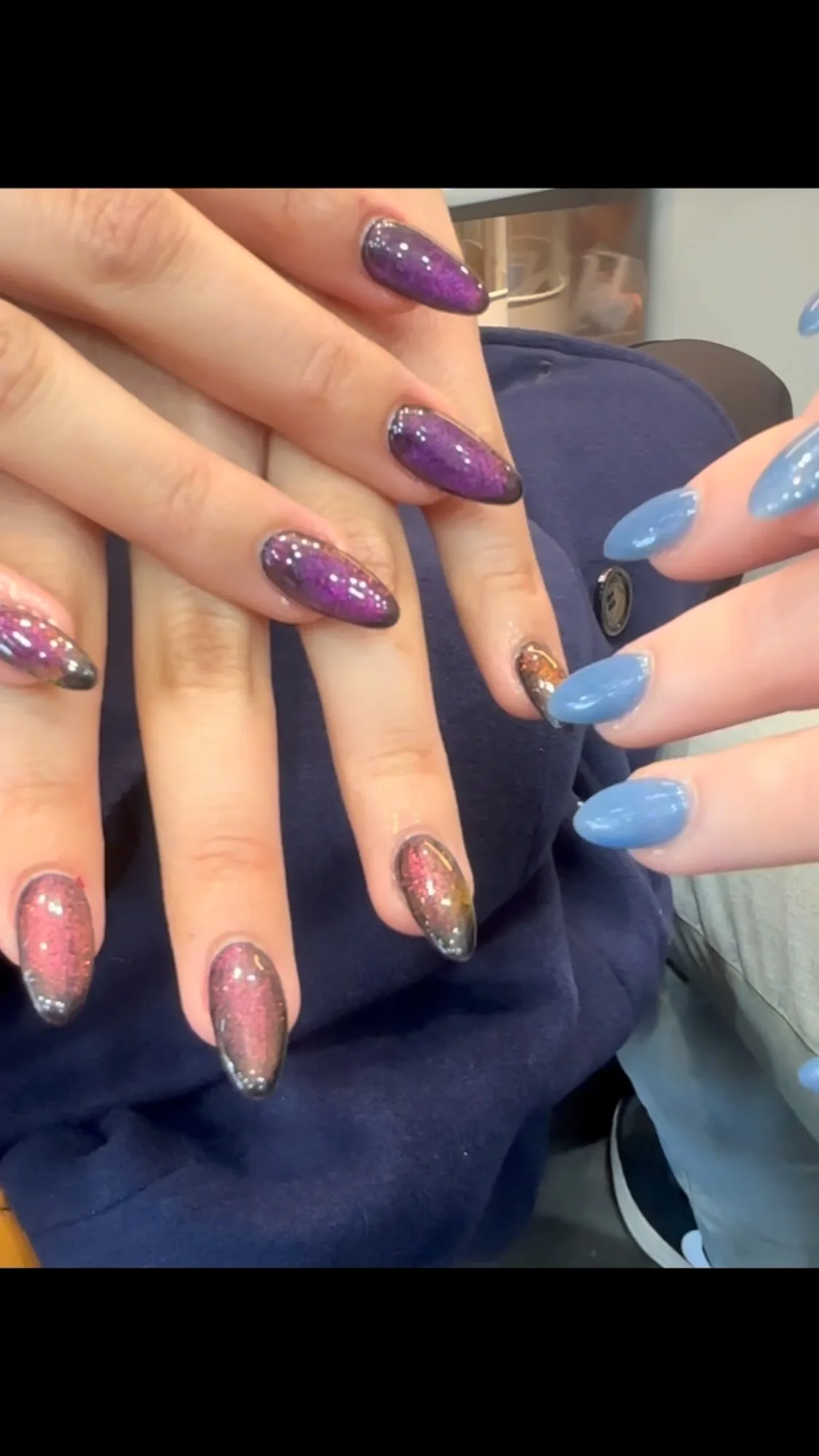 Purple and blue cat-eye galaxy shimmer nails on two hands with soft salon bokeh